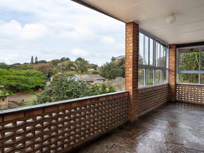 A covered balcony featuring a decorative brick balustrade, stone flooring, and expansive views of the surrounding neighborhood.