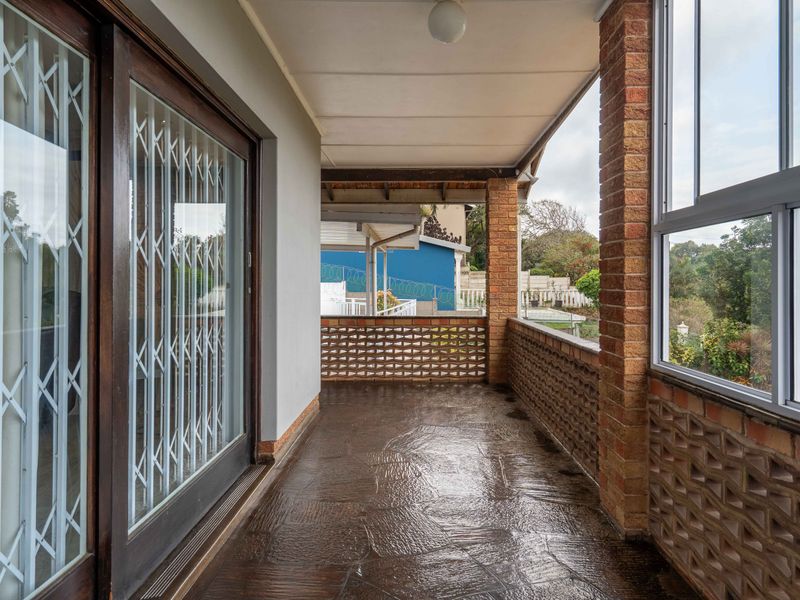 A covered patio featuring decorative brickwork balustrades, brick pillars, and a sliding glass door with security gate, offering a functional outdoor living space.