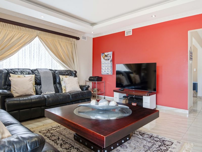 A living room featuring tiled flooring, a recessed ceiling with downlights, and a prominent red accent wall.
