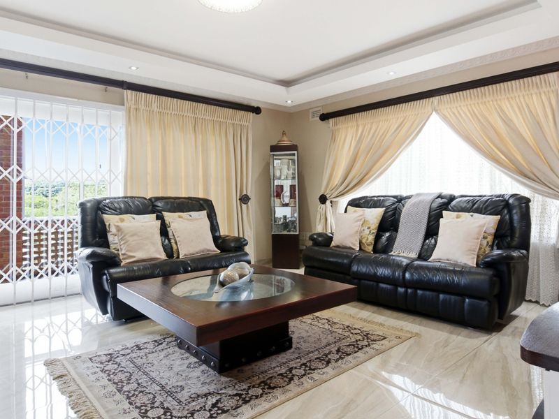 A well-maintained living room featuring polished tiled floors, recessed ceiling details, and a sliding glass door with a security gate leading outdoors.