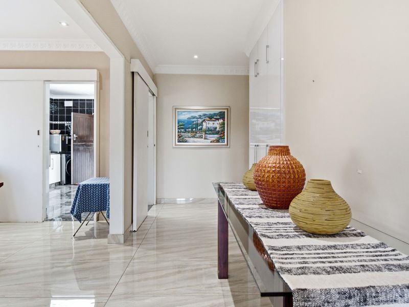 A bright, modern hallway featuring polished porcelain floor tiles, recessed downlighting, and integrated built-in storage cabinetry.