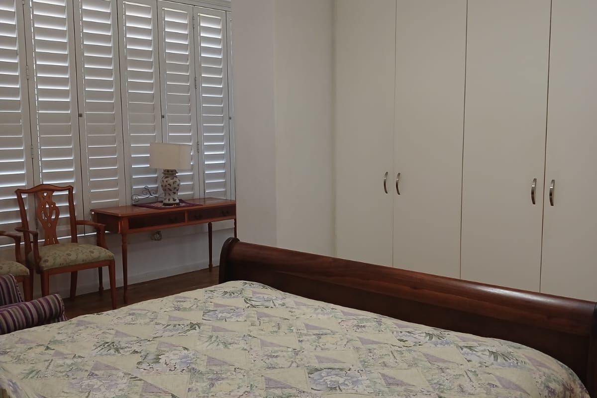 A well-maintained bedroom featuring built-in floor-to-ceiling cupboards and white plantation shutters, providing a clean and functional living space.