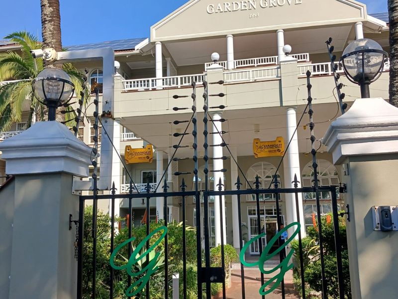 Front entrance view of Garden Grove retirement village featuring a secure gated access, paved walkway, and multi-story building facade with balcony.