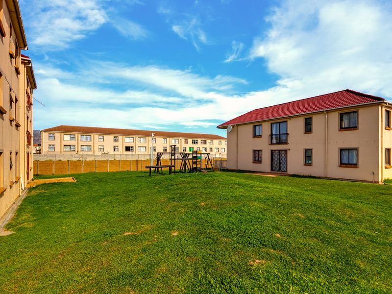 A view of the communal garden area between apartment blocks, featuring a lawn, perimeter wall, and residential building facades.