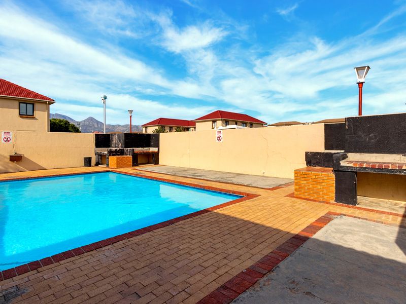 Communal pool area featuring brick paving, built-in braai facilities, and perimeter walling within an apartment complex setting.
