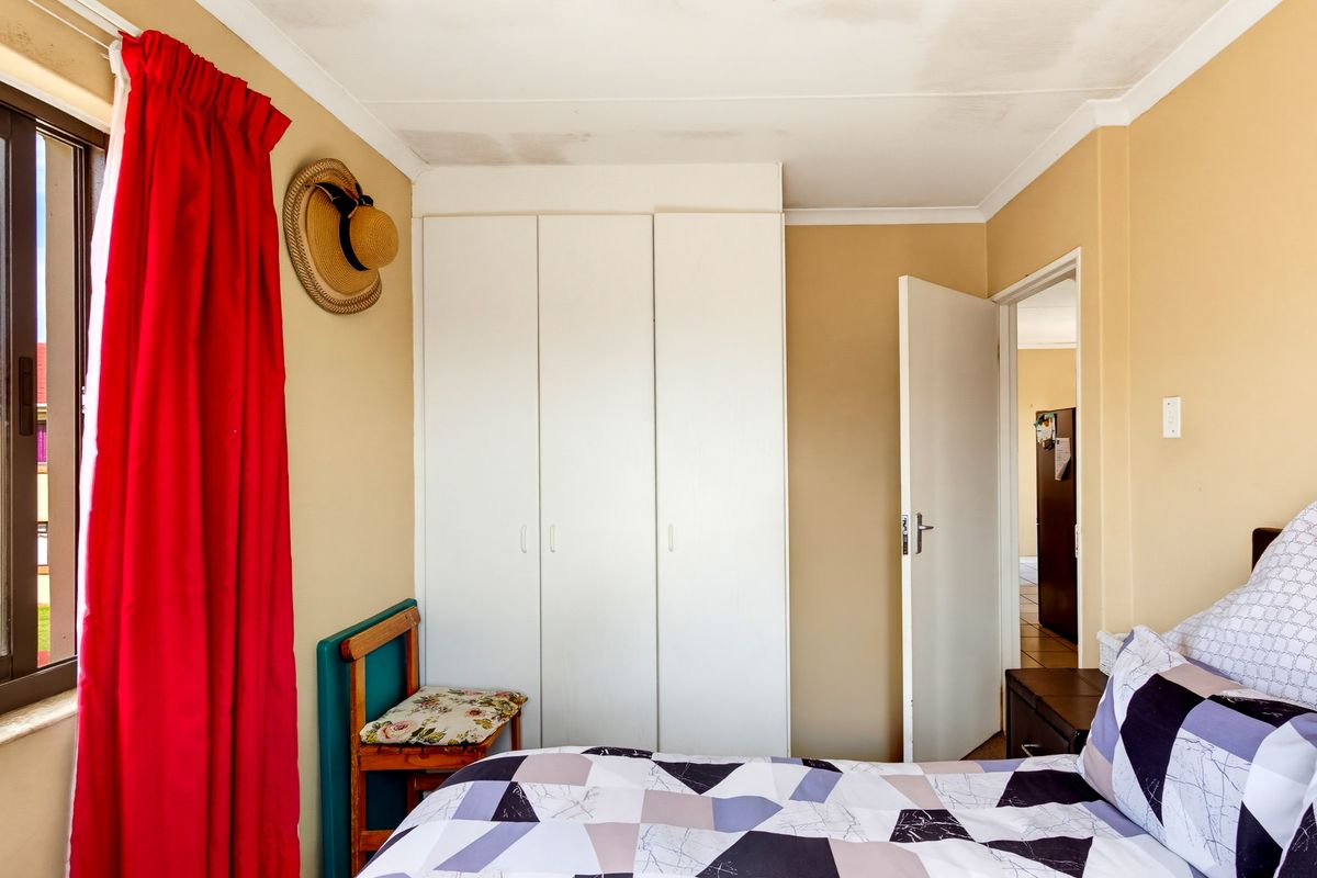 A bedroom featuring built-in cupboards and a window, showing visible signs of water staining on the ceiling.