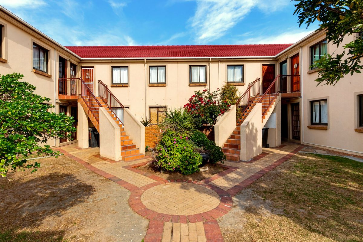 A view of the apartment complex rear courtyard featuring paved walkways, central landscaping, and external staircases leading to upper-level units.