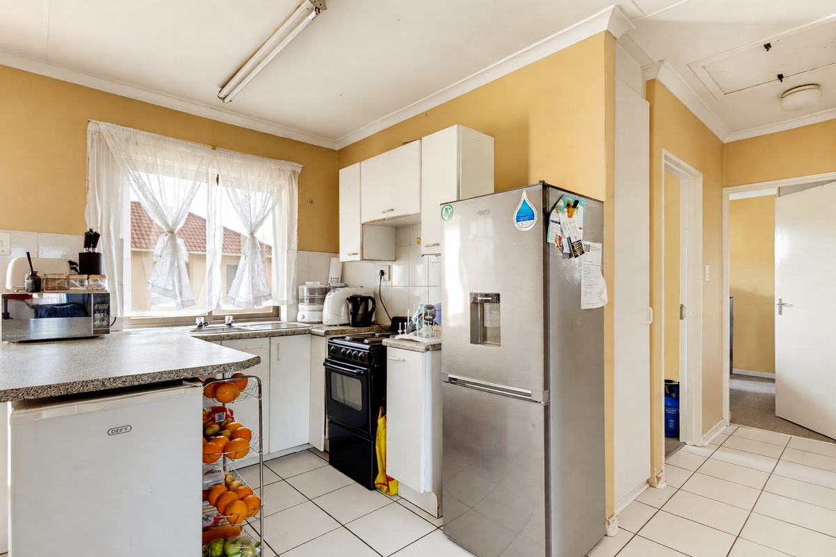 A functional kitchen featuring white cabinetry, laminate countertops, a freestanding stove, and ceramic floor tiles, offering potential for modernization and aesthetic updates.