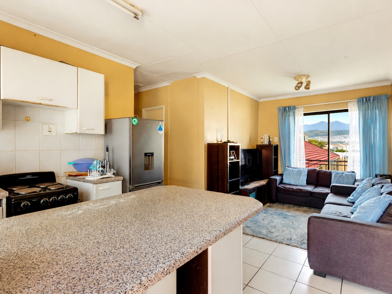 Open-plan living area featuring a functional kitchen with granite-look countertops and a bright lounge space with access to a balcony.
