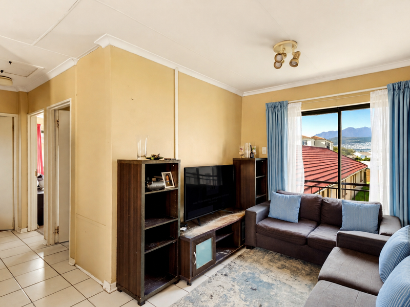 A living room featuring tiled flooring, coved ceilings, and a sliding glass door providing natural light and access to an outdoor balcony area.