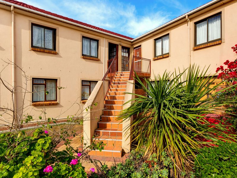 Exterior view of an apartment complex featuring a central tiled staircase leading to upper-level units with established garden landscaping.