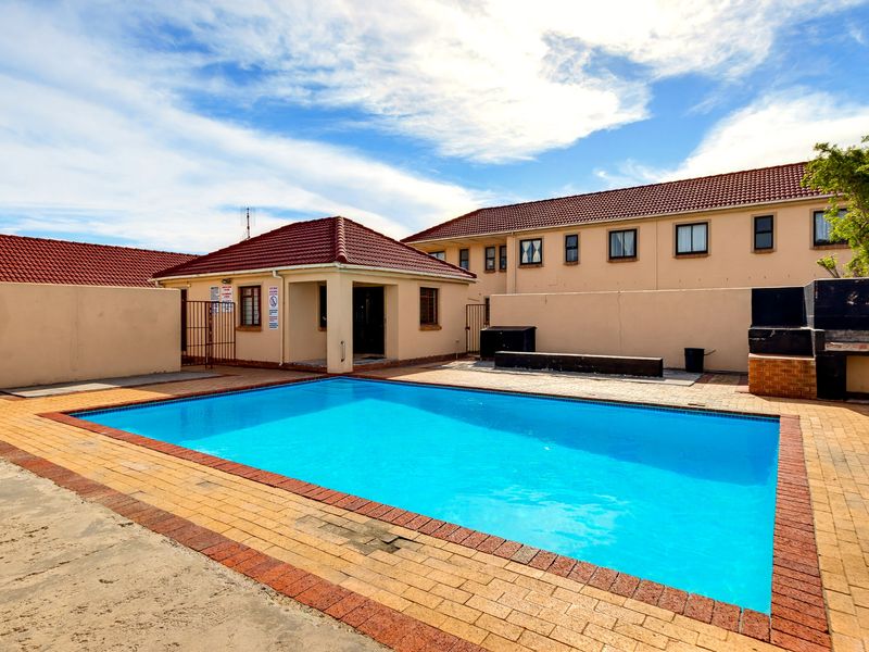 Communal swimming pool area featuring brick paving, perimeter walling, and a built-in braai facility within the apartment complex.