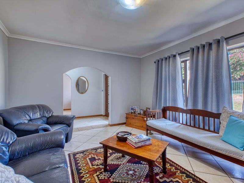 A comfortable living room featuring tiled flooring, an arched entryway, and coved cornicing, providing a neutral foundation for interior design updates.
