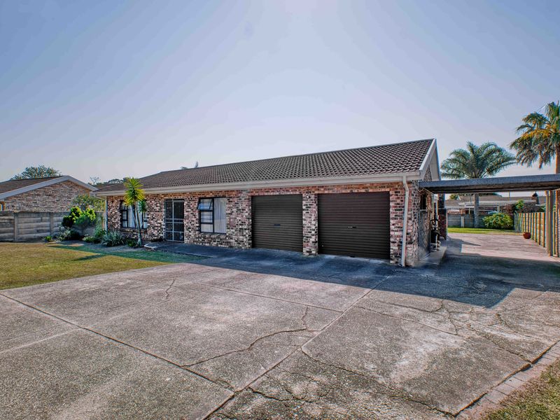 Front exterior view of a brick house featuring a double garage, attached carport, and a spacious concrete driveway.