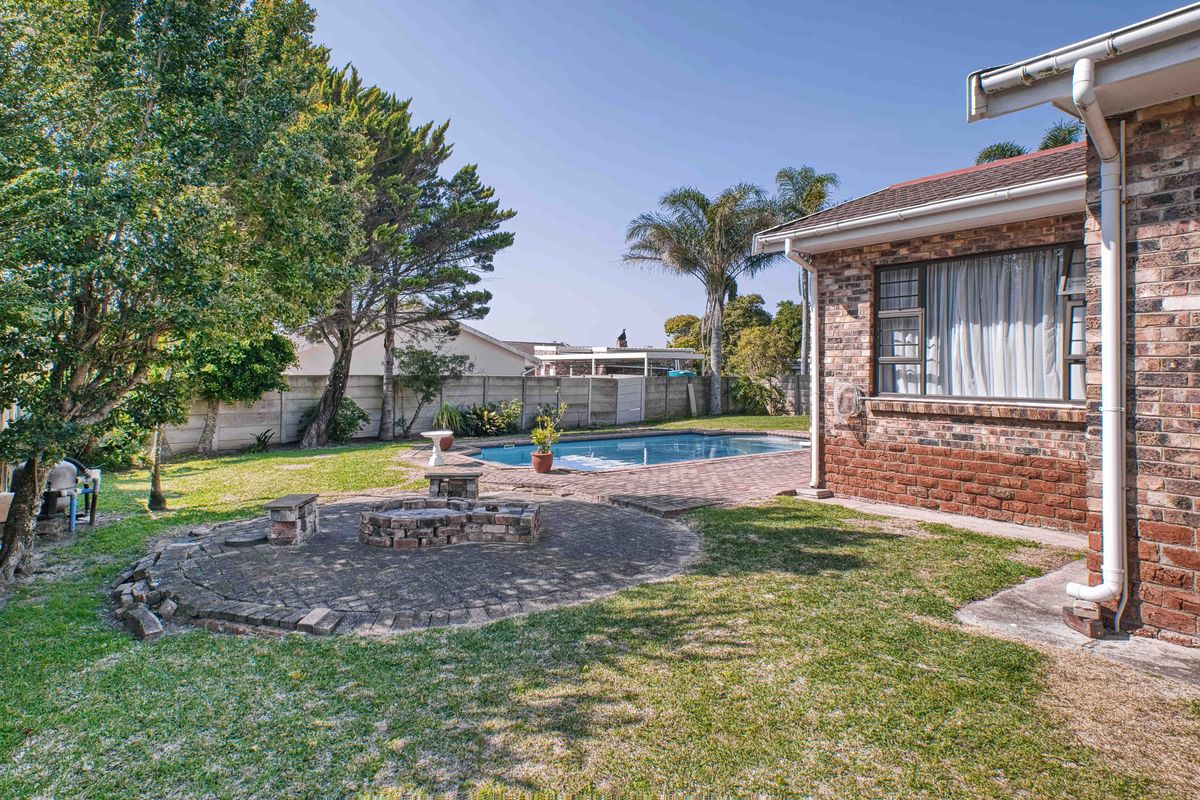 Rear garden featuring a swimming pool, brick-paved patio area with a built-in fire pit, and established landscaping enclosed by boundary walls.