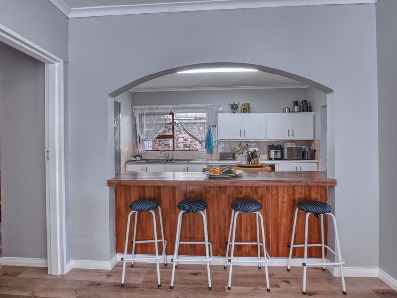 A functional kitchen featuring a tiled breakfast bar, wooden cabinetry, and a convenient archway opening into the adjacent living space.