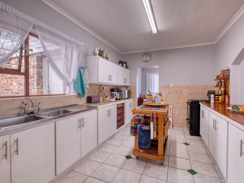 A functional kitchen featuring white cabinetry, tiled splashbacks, double stainless steel sink, and tiled flooring with a practical layout.