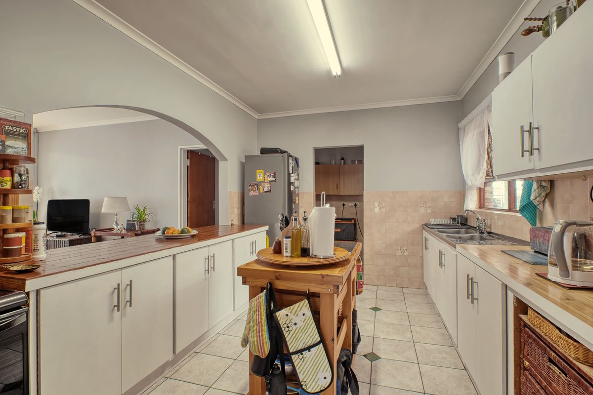 Functional kitchen featuring white cabinetry, tiled backsplash, double basin sink, and a breakfast bar opening into the adjacent living area.