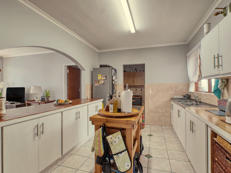 Functional kitchen featuring white cabinetry, tiled backsplash, double basin sink, and a breakfast bar opening into the adjacent living area.