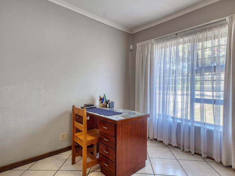 A functional office space featuring tiled flooring, neutral wall finishes, and a large window with security bars and curtain tracks.