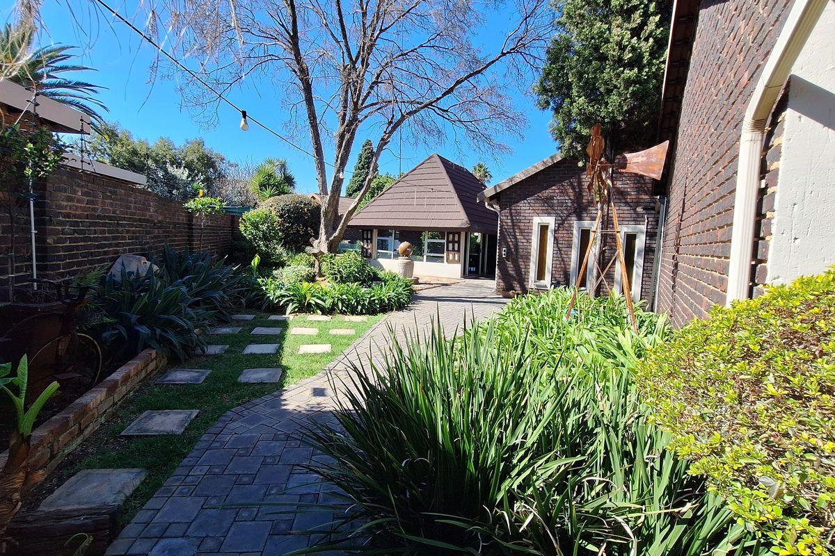 A well-maintained rear garden featuring brick paving, established landscaping, and a distinct pitched-roof outbuilding structure.