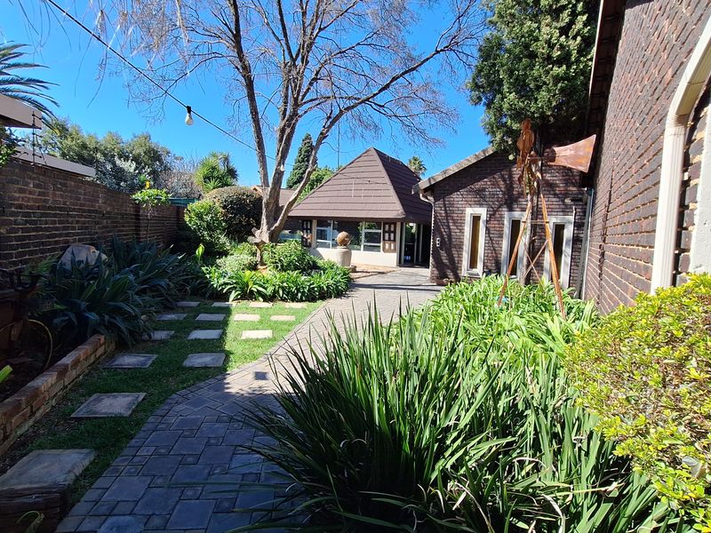 A well-maintained rear garden featuring brick paving, established landscaping, and a distinct pitched-roof outbuilding structure.