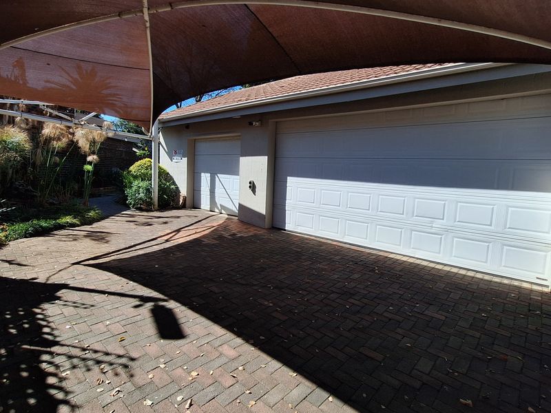 A paved driveway area featuring a double garage and a single garage, covered by a large shade sail structure.