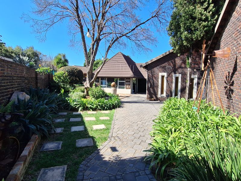A well-maintained rear garden area featuring a paved walkway, established landscaping, and brick exterior walls leading toward the main dwelling structure.