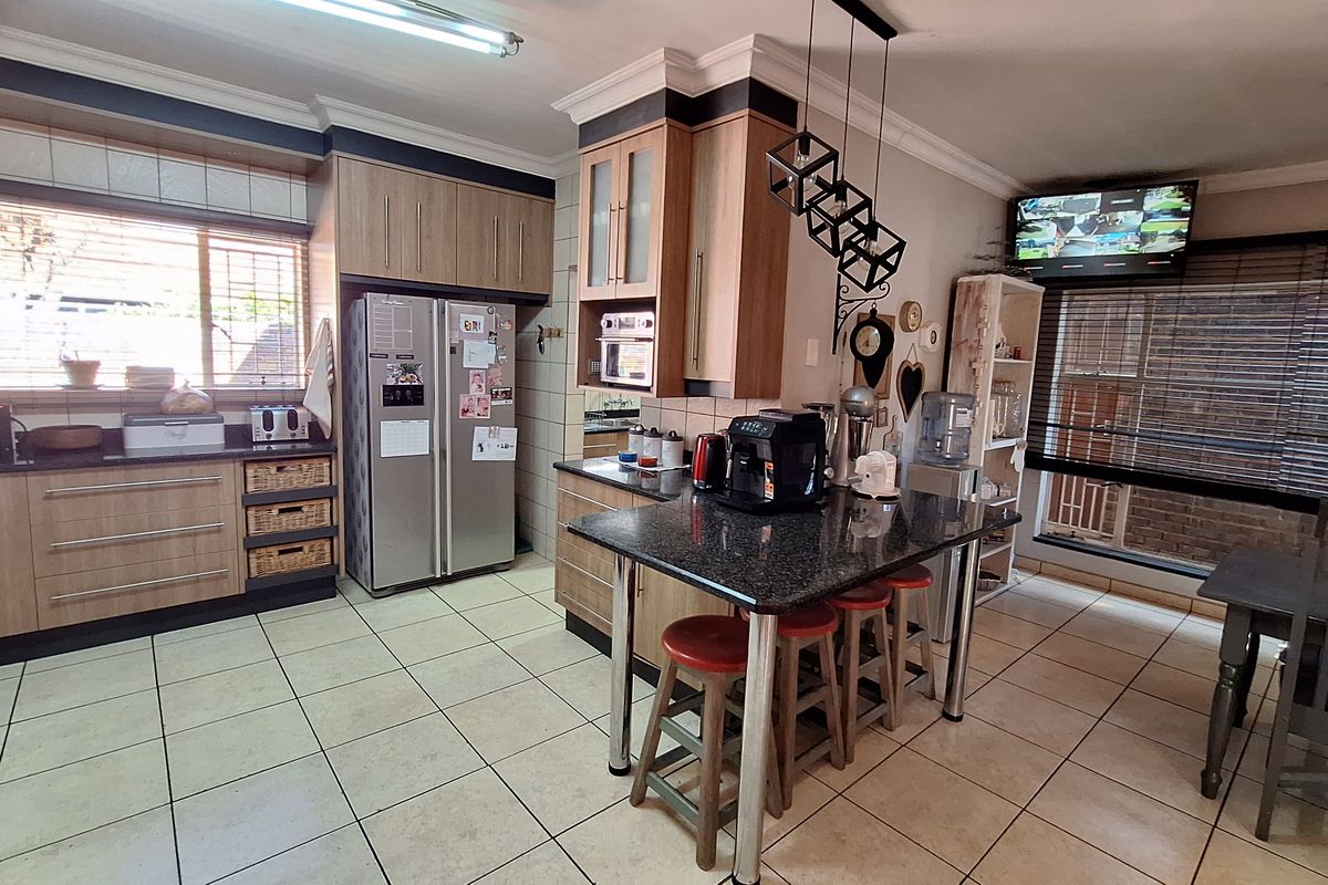 A functional kitchen featuring light wood cabinetry, granite countertops, a central island with breakfast bar seating, and ceramic floor tiles.