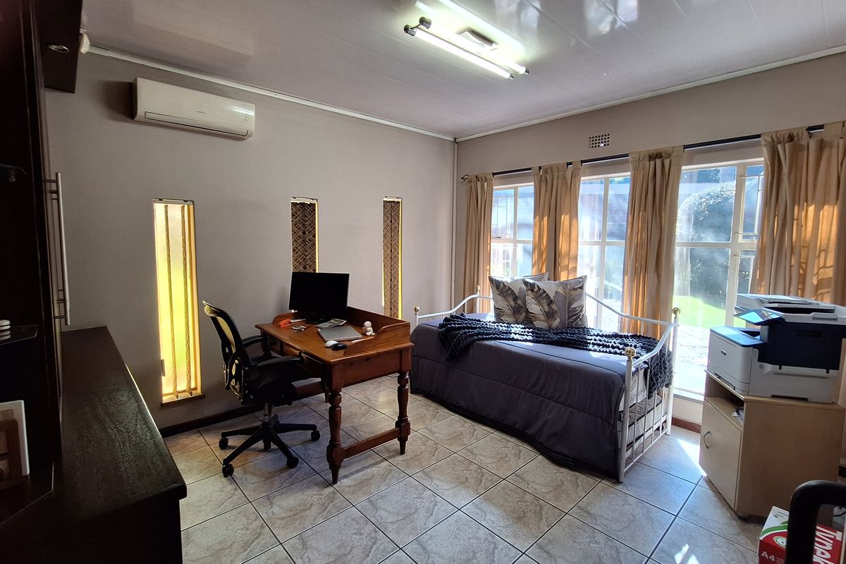 A functional bedroom or home office space featuring tiled flooring, split-system air conditioning, and large windows providing natural light.