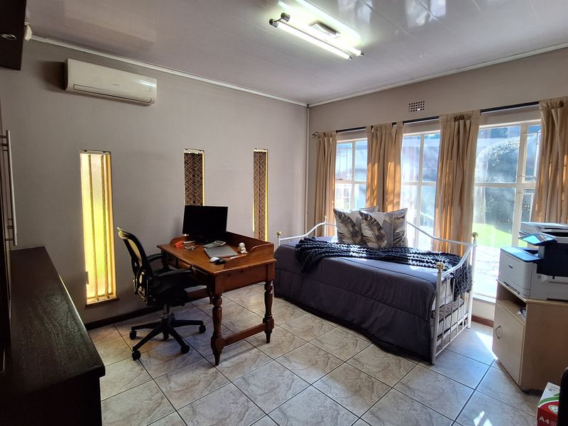 A functional bedroom or home office space featuring tiled flooring, split-system air conditioning, and large windows providing natural light.