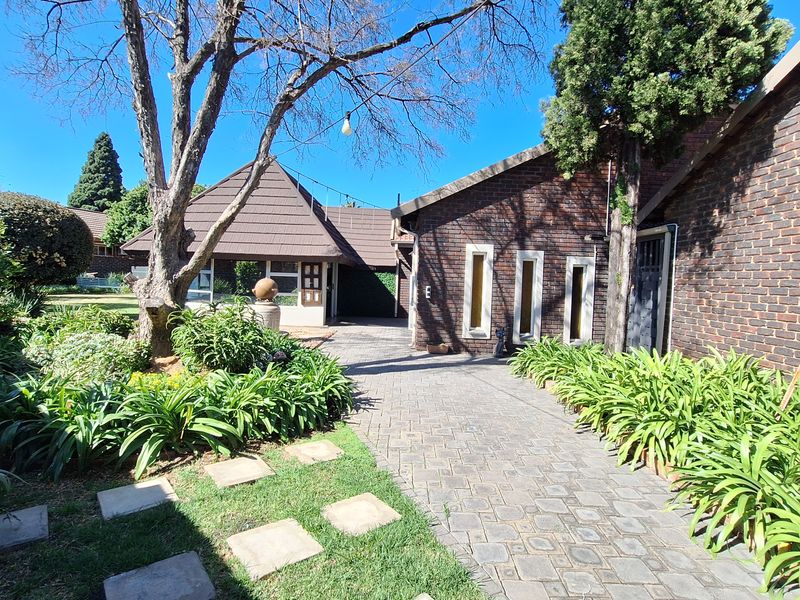 Front exterior view of a brick house featuring a paved driveway, established garden, and tiled roof architecture.