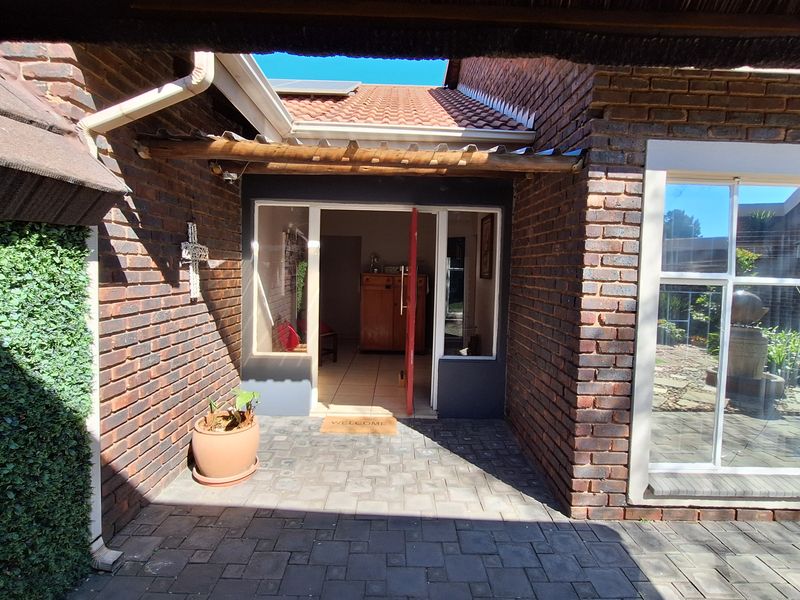 A welcoming entrance area featuring a brick facade, paved patio, and a timber pergola structure leading into the home.