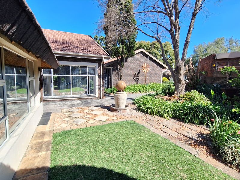 A well-maintained rear garden featuring a paved patio, stone pathways, a central water feature, and established landscaping adjacent to the main dwelling.