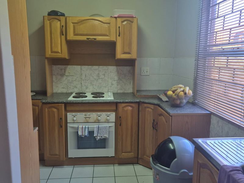A functional kitchen featuring traditional wooden cabinetry, an integrated electric hob and oven, tiled backsplash, and a stainless steel sink with natural light.