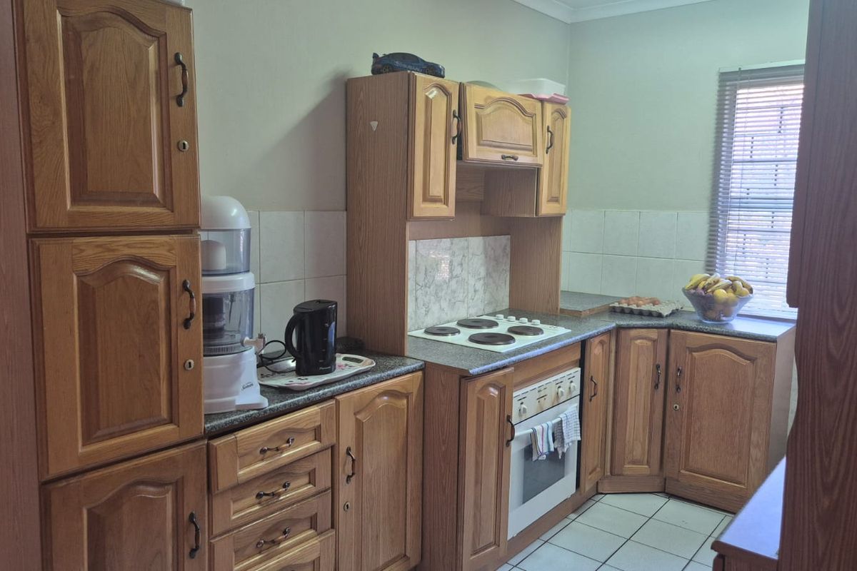 A functional kitchen featuring traditional wooden cabinetry, laminate countertops, a built-in oven, and an electric hob with tiled backsplash and flooring.