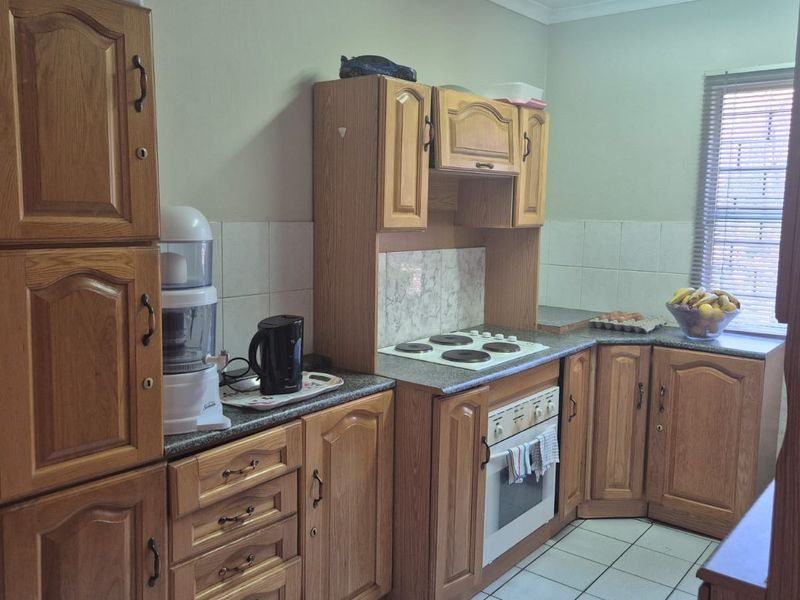 A functional kitchen featuring traditional wooden cabinetry, laminate countertops, a built-in oven, and an electric hob with tiled backsplash and flooring.