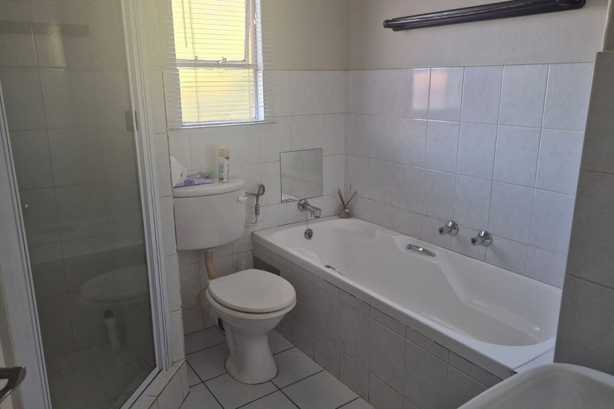 A functional bathroom featuring a shower enclosure, bathtub, and tiled finishes, offering a clean layout ready for potential cosmetic updates.