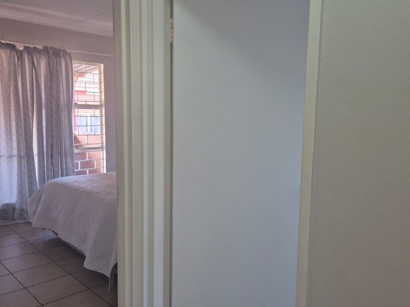 A view through a doorway into a bedroom featuring tiled flooring and a window with security bars.