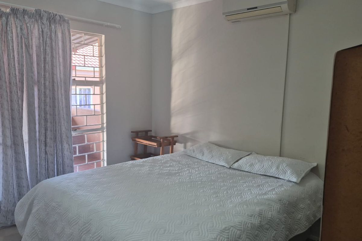A functional bedroom featuring an integrated air conditioning unit and a sliding door with security bars, providing access to an outdoor area.