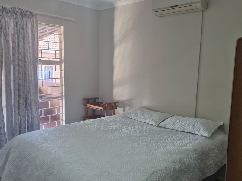 A functional bedroom featuring an integrated air conditioning unit and a sliding door with security bars, providing access to an outdoor area.