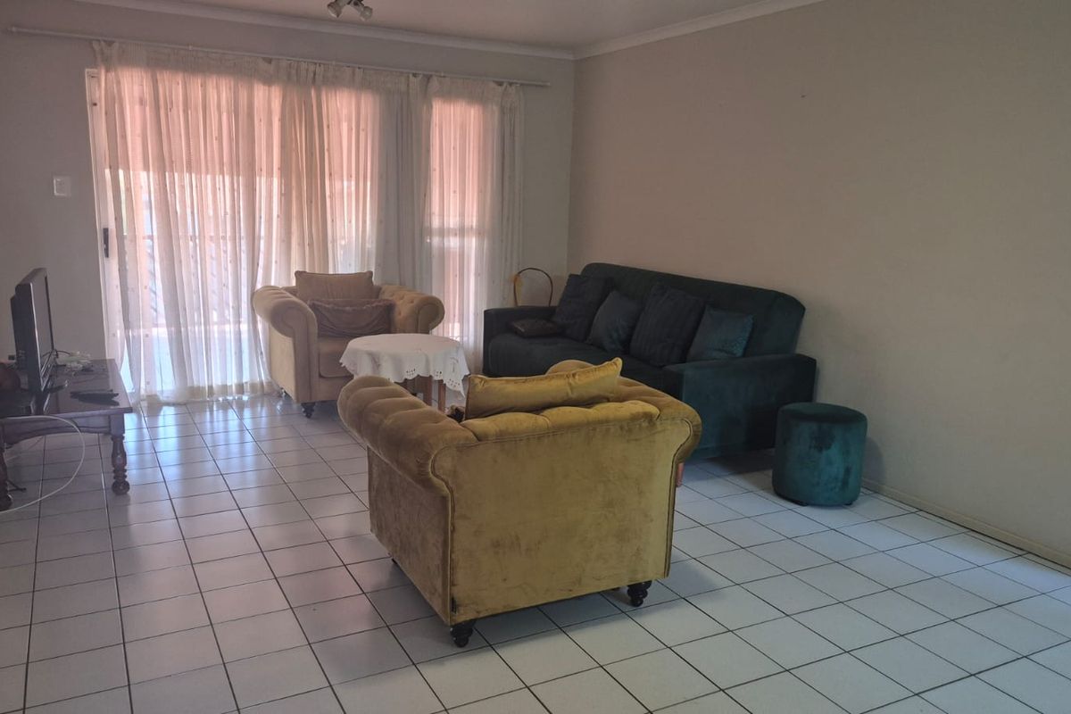 A spacious living room featuring tiled flooring, an air conditioning unit, and large sliding glass doors that provide access to the outdoor area.
