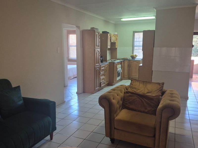 Open-plan living area featuring tiled flooring and a functional kitchen with built-in cabinetry, oven, and hob, leading to an outdoor balcony area.
