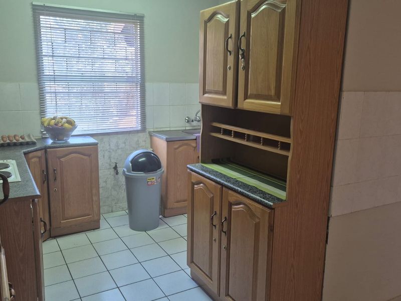 A functional kitchen featuring traditional wood-look laminate cabinetry, tiled flooring, and a tiled backsplash, offering a classic layout with ample storage space.