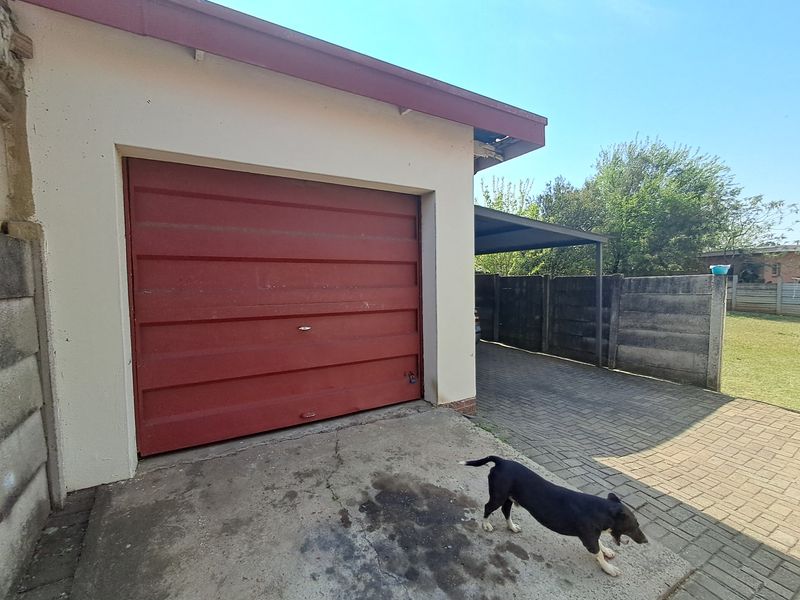 Exterior view of a single garage with a red door, adjacent paved driveway, and a carport structure.