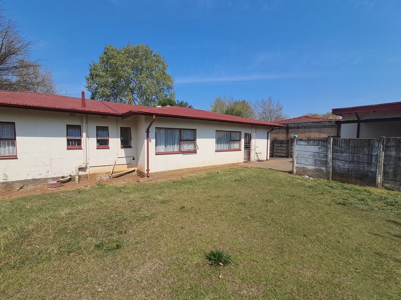 Rear view of the property featuring a corrugated metal roof, plastered exterior walls, and a private garden enclosed by a precast concrete boundary wall.