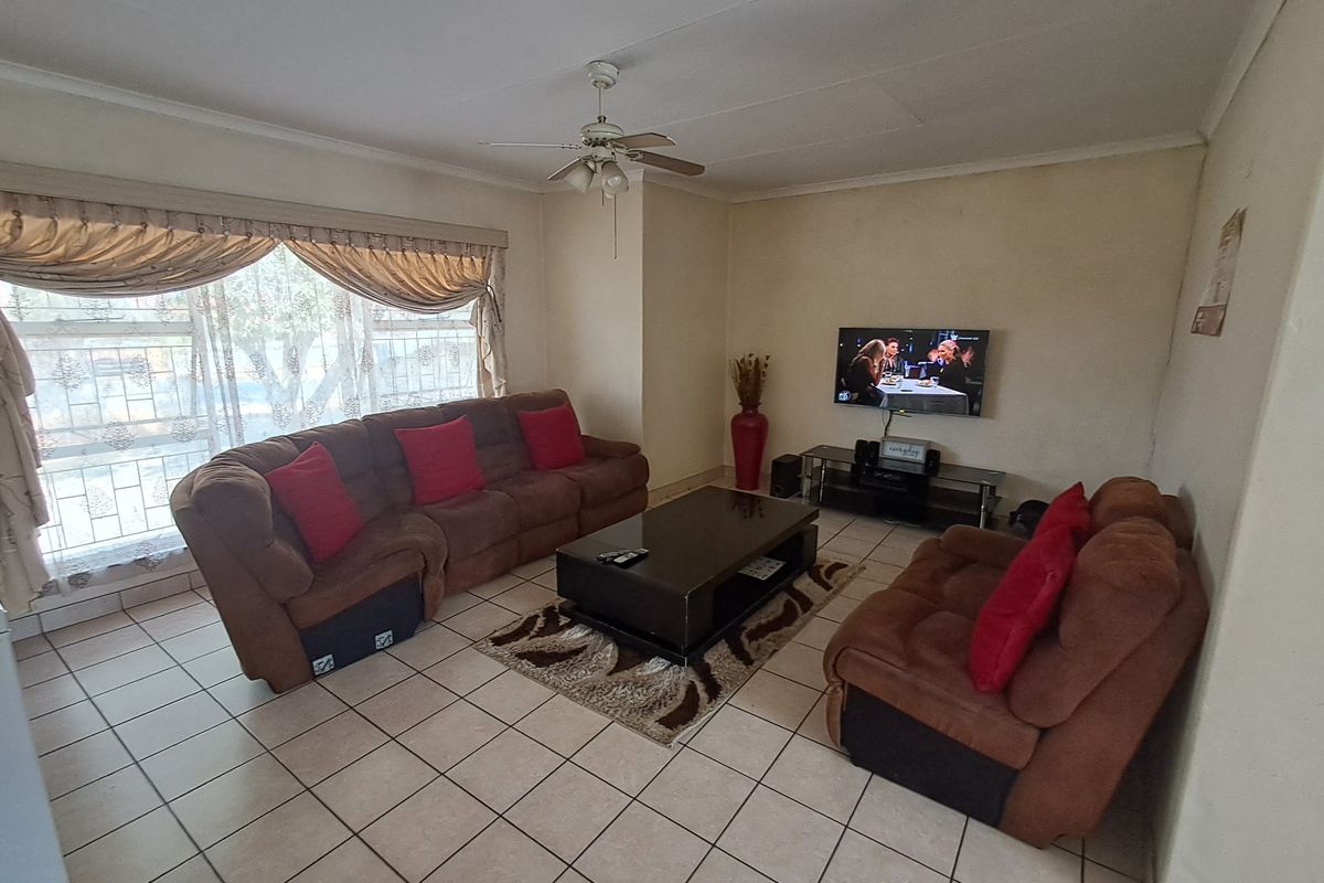 A functional living room featuring tiled flooring, a ceiling fan, and a large window providing natural light.