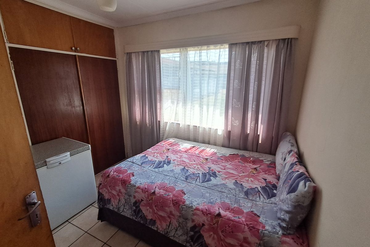 A compact bedroom featuring built-in wooden cupboards and tiled flooring, offering a functional space with potential for modernization.
