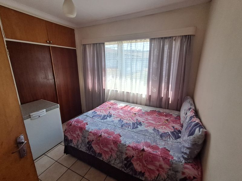 A compact bedroom featuring built-in wooden cupboards and tiled flooring, offering a functional space with potential for modernization.