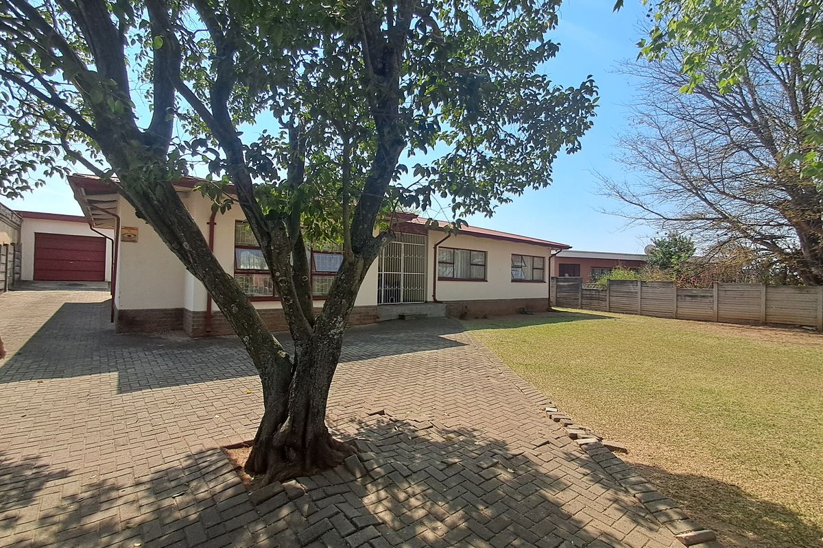 Rear view of the property featuring a paved driveway, a spacious lawn, and a secure perimeter wall.